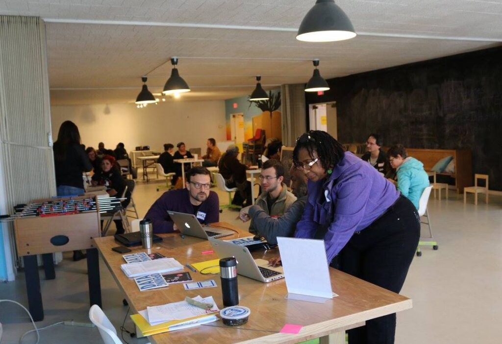 Participants at the Data Security Discotech gathered around laptops in small groups in a large room