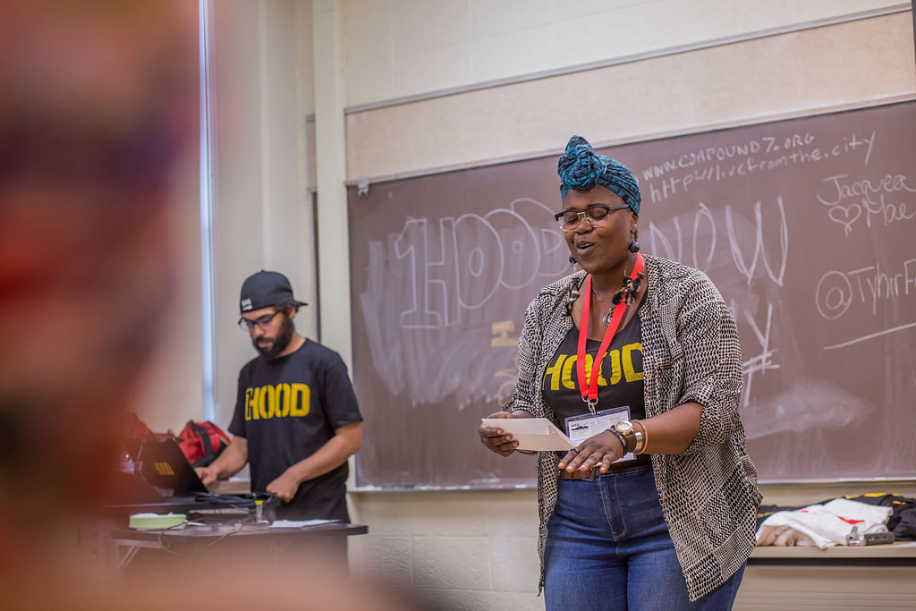 Performer from 1Hood in the front of classroom with another person supporting on a laptop