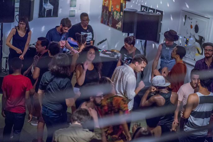 People dancing in an art gallery near a DJ