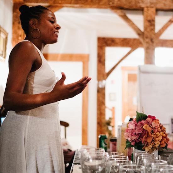 Cornetta standing at a table with glasses and flowers, speaking with hand guestures