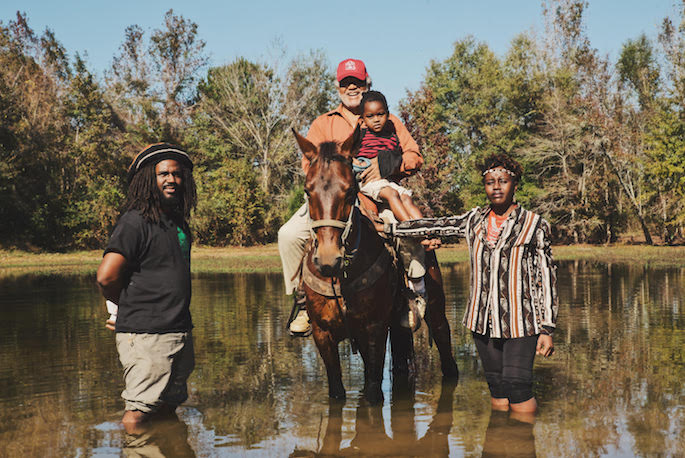A still from the documentary "Sidelots" of an intergenerational family, the eldest and youngest sitting on a horse, all in knee deep water