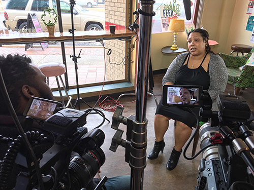 Production still from Take Me Home of a person on camera sitting in a shop